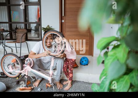 Père et fille souriant entre les rayons de roue de vélo Banque D'Images