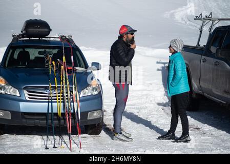 Un homme et une femme en conversation se tiennent face à face près de leur voiture et de leur camion dans un parking couvert de neige. Banque D'Images