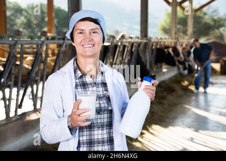 fermier en robe blanche posant le fond des vaches dans la cabine avec le lait Banque D'Images