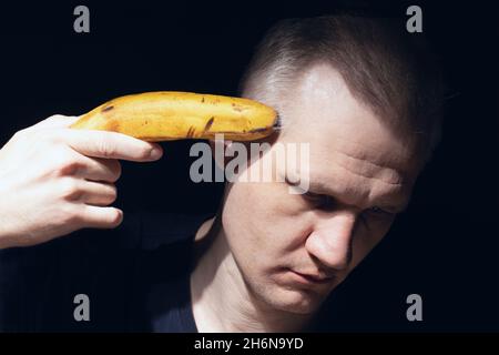 L'homme tient la banane près de sa tête comme pistolet gros plan sur fond noir.Prenez votre photo avec une banane.Désespoir, dépression et pensées suicidaires.Mental Banque D'Images