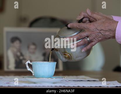 Photo générique d'une vieille main femelle versant une tasse de thé d'un pot dans une tasse de porcelaine. Banque D'Images