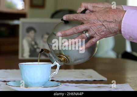 Photo générique d'une vieille main femelle versant une tasse de thé d'un pot dans une tasse de porcelaine. Banque D'Images