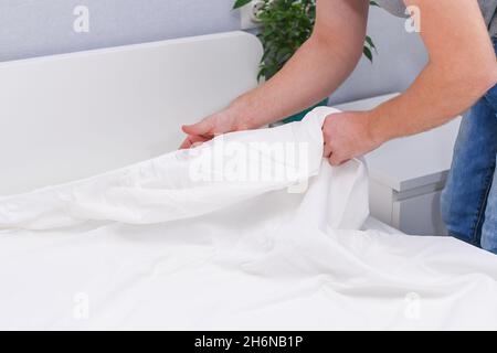 Un homme met un drap élastique sur le matelas.Changement du linge de lit. Banque D'Images