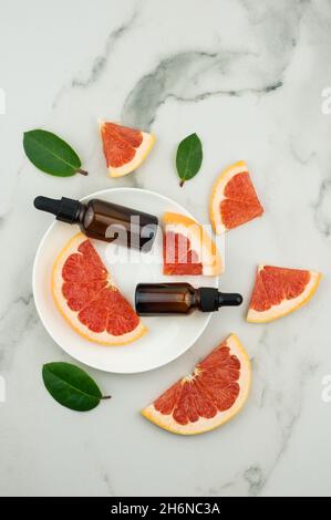 vue de dessus d'une assiette blanche avec deux flacons compte-gouttes avec huile de pamplemousse et tranches de fruits. effet hydratant, aromatherapy, anti-stres Banque D'Images