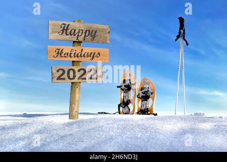 Bonne année 2022 écrit sur une affiche plantant dans la neige à côté de raquettes et de bâtons sous le ciel bleu Banque D'Images