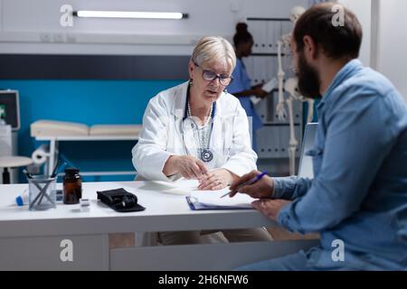 Le patient lors d'une visite médicale signe les papiers de contrôle pour le médecin et le rendez-vous.Un spécialiste des soins de santé demande la signature des documents pour l'homme, donnant un traitement contre le diagnostic en cabinet. Banque D'Images