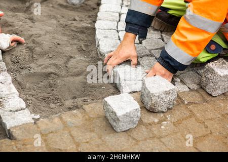 Travaux d'entretien sur le pavage avec pavés emboîtés.Personnes non reconnaissables avec des matériaux de construction en main, des produits en béton, un dégoût de bâtiment Banque D'Images