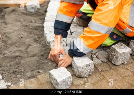 Travaux d'entretien sur le pavage avec pavés emboîtés.Personne méconnaissable avec des matériaux de construction en main, des produits en béton, l'industrie du bâtiment Banque D'Images