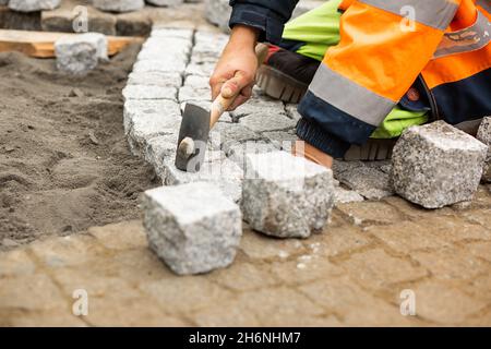 Travaux d'entretien sur le pavage avec pavés emboîtés.Personne méconnaissable avec des matériaux de construction en main, des produits en béton, l'industrie du bâtiment Banque D'Images