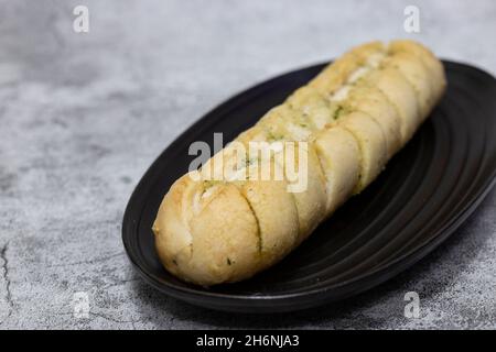 Baguette à pain à l'ail et aux herbes sur une assiette en granit noir.Sur un fond concret Banque D'Images