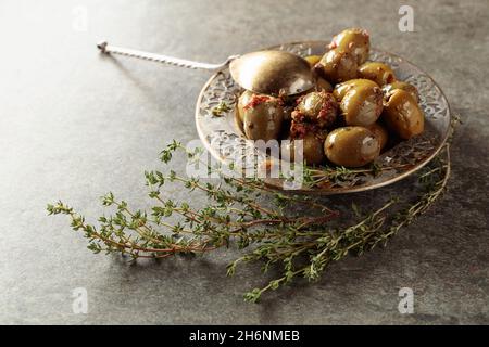 Olives vertes épicées à l'huile d'olive dans un ancien bol en métal.Bol avec olives et brindilles de thym sur une table en pierre. Banque D'Images