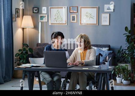 Aidez volontairement une femme âgée à utiliser un ordinateur pendant qu'elle est assise à la table dans le salon Banque D'Images