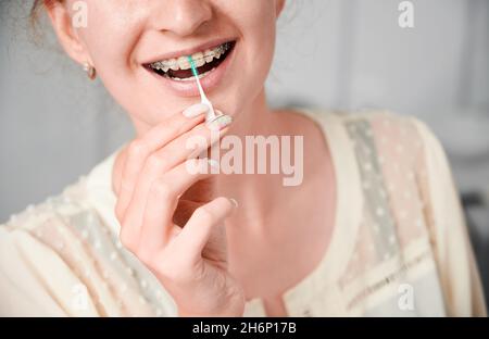 Gros plan d'une jeune femme souriante utilisant une brosse dentaire tout en nettoyant les dents avec des bretelles.Femme avec supports orthodontiques se brossant les dents avec un cure-dent élastique.Concept de dentisterie, hygiène Banque D'Images