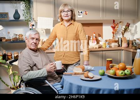 Portrait d'un couple senior regardant l'appareil photo tout en prenant le petit déjeuner à la table dans la cuisine Banque D'Images