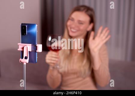 femme tient le verre de vin en main et les vagues main à l'appareil photo du téléphone. mise au point sélective, mise au point au premier plan, faible profondeur de champ photo Banque D'Images
