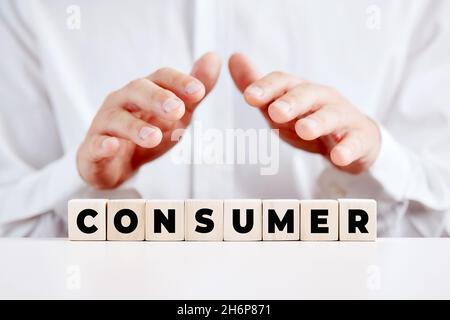 Les mains de la personne d'affaires couvrant le mot consommateur écrit sur des cubes en bois.Concept d'assistance, de satisfaction ou d'assistance à la clientèle ou à la clientèle. Banque D'Images