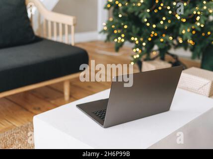 Ordinateur portable ouvert sur la table dans la salle de séjour avec arbre de Noël décoré, concept de shopping en ligne Banque D'Images