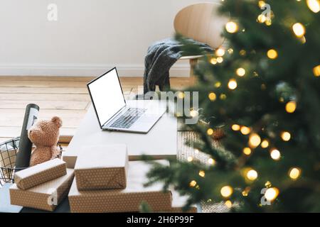 Ordinateur portable ouvert sur la table dans la salle de séjour avec arbre de Noël décoré, concept de shopping en ligne Banque D'Images