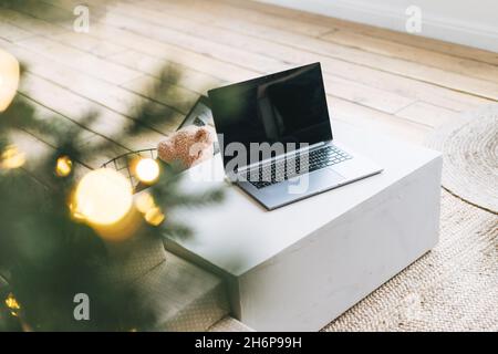 Ordinateur portable ouvert sur la table dans la salle de séjour avec arbre de Noël décoré, concept de shopping en ligne Banque D'Images