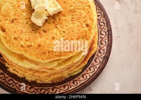 Des crêpes ou des crêpes minces s'empilent avec du beurre et du caviar rouge sur une belle plaque en céramique sur un fond de béton brun ancien. Vue de dessus, espace de copie. Homemad Banque D'Images