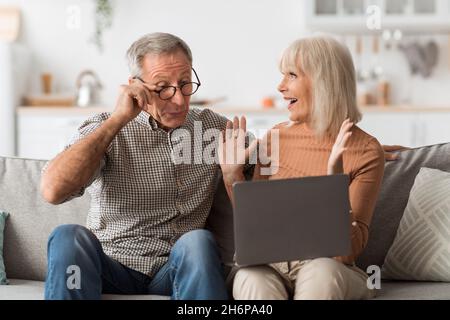 Joyeux conjoint senior regardant l'ordinateur portable célébrant le succès à la maison Banque D'Images
