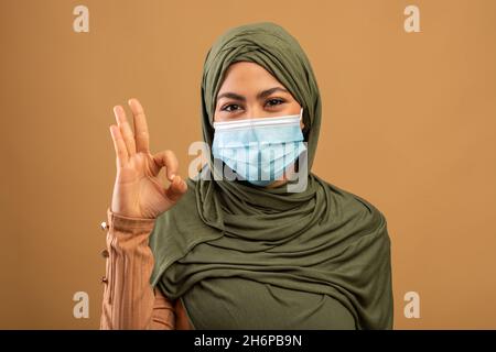 Protection contre les maladies.Femme musulmane dans le hijab portant un masque médical de protection, posant sur fond marron Banque D'Images