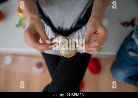 Vue de dessus d'une femme nouant une ficelle dorée à une boule de noël brillante. Banque D'Images