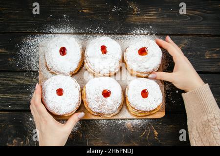 Cuisine traditionnelle Hanukkah sufganiyot.Femme saupoudrer les beignets avec du sucre en poudre.La main tient Berliner avec de la confiture. Banque D'Images