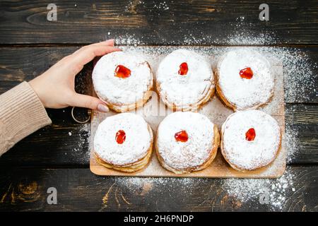 Cuisine traditionnelle Hanukkah sufganiyot.Femme saupoudrer les beignets avec du sucre en poudre.La main tient Berliner avec de la confiture. Banque D'Images