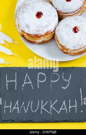 Happy Hanukkah. Jewish dessert Sufganiyot on yellow background. Symbols of religious Judaism holiday. Donuts, candles and gifts. Stock Photo