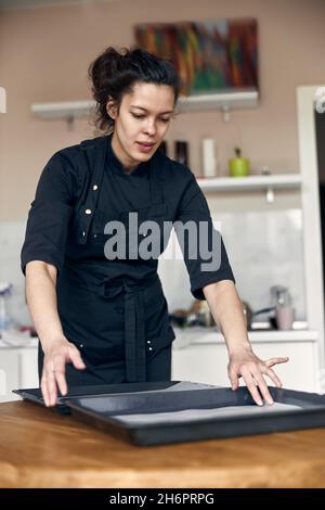 jeune belle femme de race mixte de papier de pâtisserie sur un plat dans la cuisine moderne claire Banque D'Images