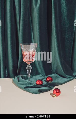 Direction artistique vintage créative.Composition minimale pour le nouvel an ou la fête de Noël avec boules rouges et verre à cocktail sur fond vert et sable coloré Banque D'Images