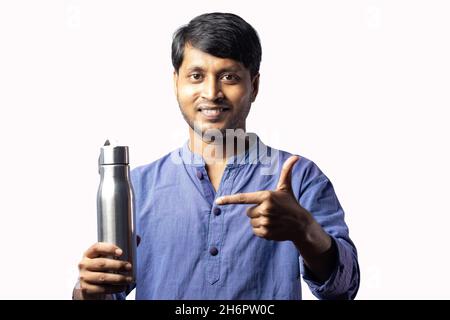 Un Indien d'âge moyen pointant vers une bouteille en acier inoxydable à la main sur fond blanc Banque D'Images