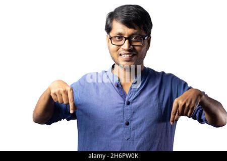 Un jeune indien en robe bleue pointant vers le bas avec les deux mains sur fond blanc Banque D'Images
