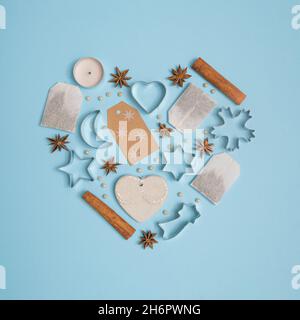 Arrangement en forme de coeur fait de sachets de thé, bâtons de cannelle, graines d'anis, bougie et moules à biscuits sur fond bleu.Un amour minimal et créatif pour l'hiver Banque D'Images