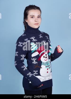 Brunette dame dans un pull bleu du nouvel an avec un bonhomme de neige sur fond bleu Banque D'Images