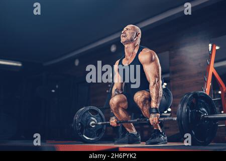 Bodybuilder musclé homme faisant un exercice lourd de deadlift avec le poids pendant que dans la salle de gym dans l'obscurité Banque D'Images