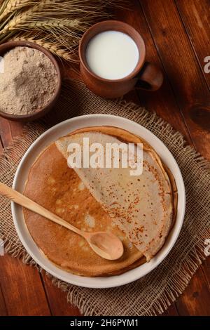 Des galettes de sarrasin traditionnelles bretons sur une table avec de la farine, une plante de blé et du lait Banque D'Images