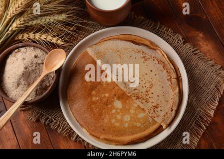 Des galettes de sarrasin traditionnelles bretons sur une table avec de la farine, une plante de blé et du lait Banque D'Images