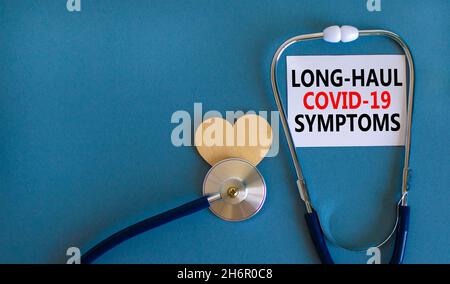 COVID-19 symbole symptômes de covid long-courrier.Carte blanche avec mots long-haul covid-19 symptômes.Coeur en bois, stéthoscope, fond bleu, espace de copie.M Banque D'Images