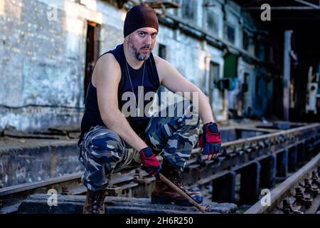 Un jeune rebelle dans un hall d'usine abandonné avec une barre de métal dans sa main, se brouiller et regarder avec haine la caméra.Mise au point sélective. Banque D'Images