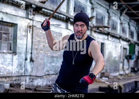 Un jeune rebelle dans un hall d'usine abandonné avec une barre de métal dans sa main, menaçant et regardant avec haine la caméra.Mise au point sélective. Banque D'Images