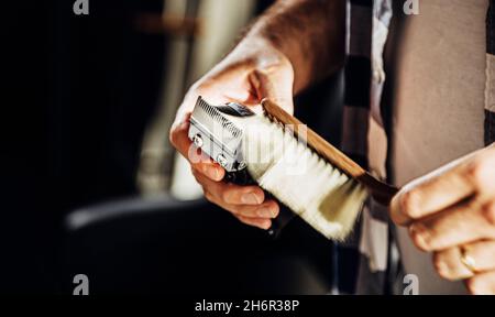 Coiffeur nettoyant une tondeuse à cheveux avec une brosse. Banque D'Images