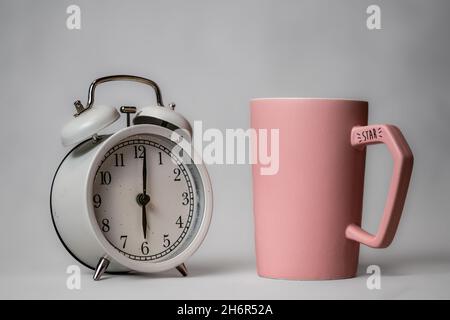 Un réveil noir de style rétro et une tasse de café rose sur une petite soucoupe se tiennent sur un fond.Concept Bonjour.Café du matin Banque D'Images