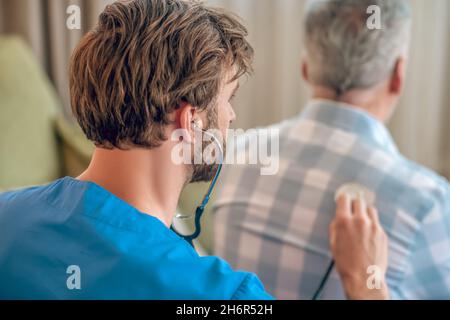 Médecin qualifié aux cheveux foncés auscultant un homme aux cheveux gris Banque D'Images