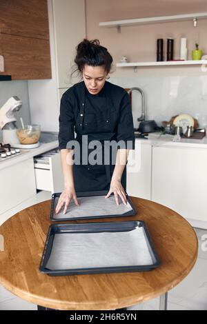 jeune belle femme de race mixte de papier de pâtisserie sur un plat dans la cuisine moderne claire Banque D'Images