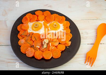 visage amusant composé de carottes sautées et d'œufs frits sur une plaque en céramique noire Banque D'Images