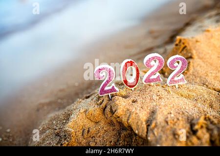 Figures 2022 sur fond de vagues côtières par océan ou mer avec canne au caramel.Voyage en quarantaine le jour de la Saint-Sylvestre, avant l'arrivée du nouveau Banque D'Images