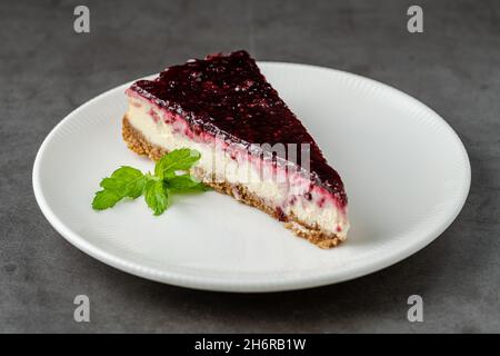 Cheesecake à la framboise sur une assiette blanche sur une table en pierre sombre Banque D'Images