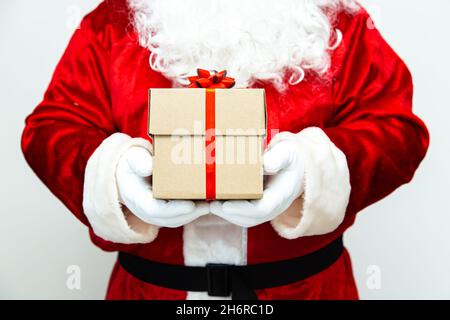 Le Père noël a des mains gantées tenant une boîte cadeau avec un ruban rouge. Banque D'Images